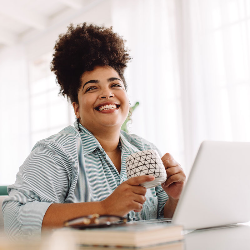 Mirjam Quinn Training Department, woman smiling while drinking coffee at her computer