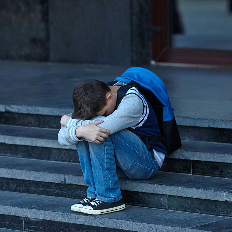 School Refusal Program MQA, young student with a backpack holding their head in their hands looking depressed on stairs